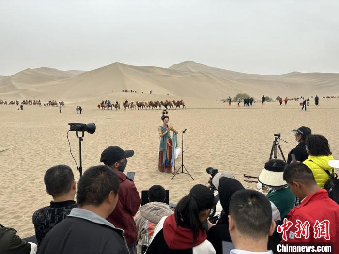 圖為2023年4月底，敦煌大漠“逐舞者”奧楠在鳴沙山月牙泉景區(qū)視頻直播，吸引游人圍觀?！●T志軍 攝