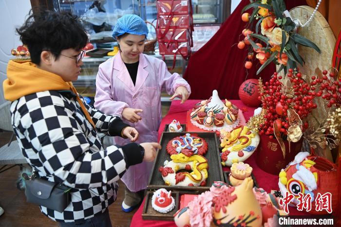 1月25日，隨著春節(jié)臨近，蘭州一花饃店“龍”元素花饃熱銷。圖為工作人員向顧客推薦“龍”元素花饃。九美旦增 攝</p><p>